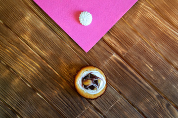 Round fruit cream cake and meringue on the table from pine planks. Minimalism. Natural brown and pink background. View from above