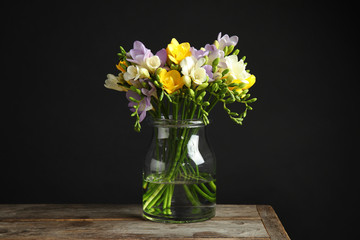 Bouquet of fresh freesia flowers in glass vase on table against black background