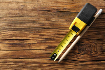 Metal measuring tape and pencil on wooden background, top view. Space for text