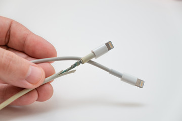 A hand holds two wires with a lightning connector. One wire is working, the other wire is damaged