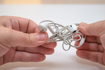male hands are holding white headphones with tangled wires