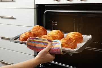 Woman taking freshly baked buns out of oven, closeup
