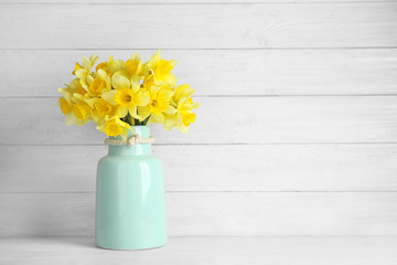 Bouquet of daffodils in vase on table against wooden background, space for text. Fresh spring flowers