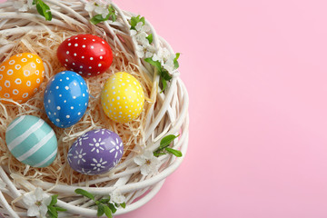 Nest with painted Easter eggs and space for text on color background, top view