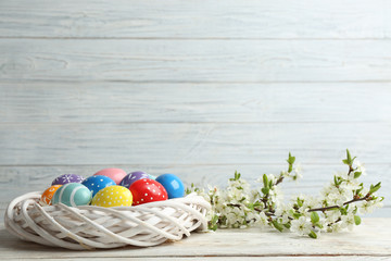 Painted Easter eggs in nest and blossoming branches on table. Space for text