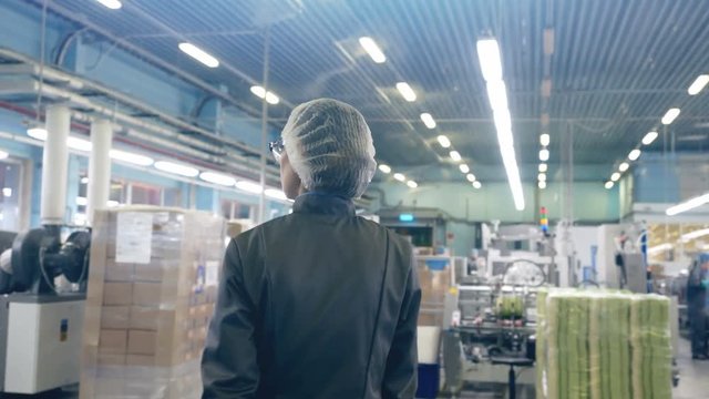 Back view of female worker in printing house, walking through equipment, following her team.