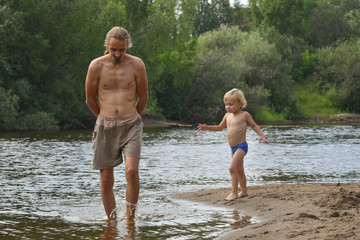 Fototapeta premium Father and son on the beach. Happy family. river. happy family on the beach. swimming. hot summer day. vacation. coach. father's day. blond boy.