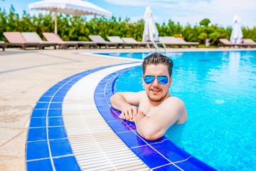 Man looks out of the pool, hanging on the railing.