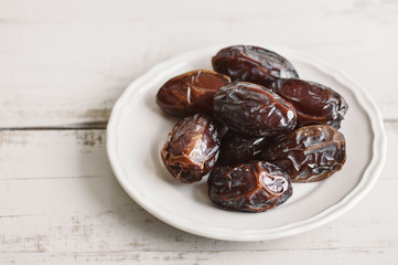 Dried dates in a white small plate on wooden table. Traditional sweet food in the Middle East