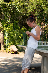 A teenager girl is waiting for someone near the table tennis on the playground on a summer, sunny day.