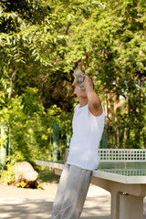 Teen girl drinks water from a bottle near a table tennis on the sports field on a summer, sunny day.