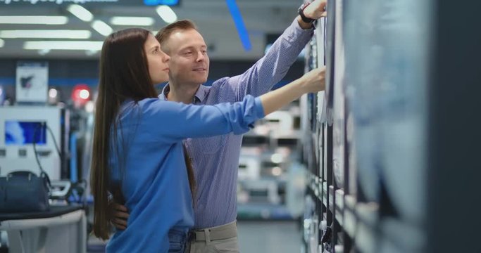 A handsome man and a woman choose a washing machine to buy open the door and inspect the coating of the drum and the quality of the product. A woman looks inside the washing machine. The purchase of a