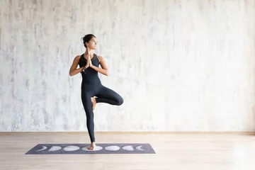 Keuken foto achterwand Yogaschool Beautiful young brunette woman yoga instructor doing vrikshasana on a mat in a wooden floor standing in the gym with day lighting