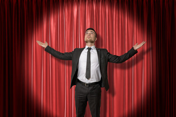 Happy young businessman standing and looking up with arms spread out to the side lit up by...