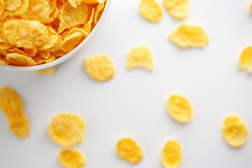 White cup with golden corn flakes, isolated on white background. Hopya crumbled around the cup. View from above