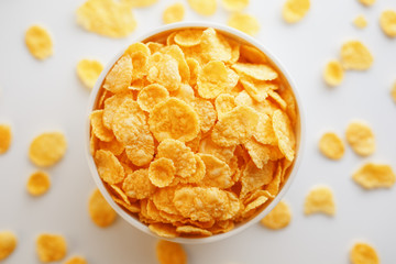 White cup with golden corn flakes, isolated on white background. Hopya crumbled around the cup. View from above