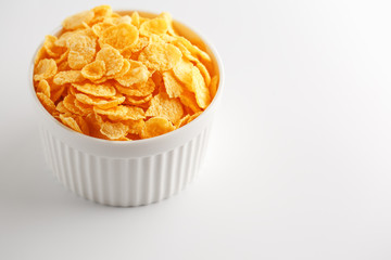 White cup with golden corn flakes isolated on white background. View from above. Delicious and healthy breakfast