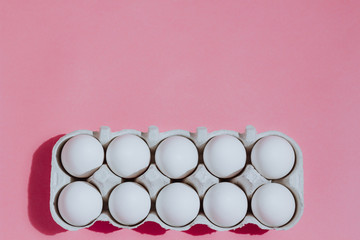 White chicken eggs in a cardboard package with empty space, on a pink background