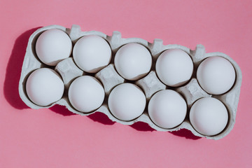 White chicken eggs in a cardboard package with empty space, on a pink background
