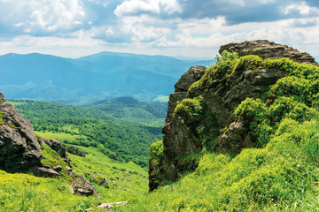 summer nature landscape in mountains. huge boulders on the edge of a grassy slope. ridge behind the valley in the distance. sunny weather with cloudy sky. beautiful carpathian scenery