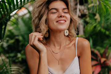 Fototapeta premium Romantic happy woman with short hair closed eyes and enjoying vacation in summer day on background of exotic plants 
