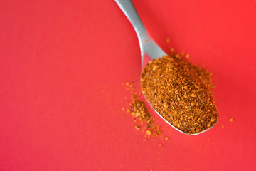 Spoonful of Dry Ground Peppers - Chili - on red background
