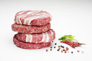 Raw meat patties with spices for burgers on a white background.