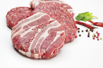 Raw meat patties with spices for burgers on a white background.