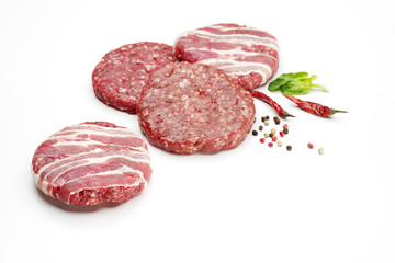 Raw meat patties with spices for burgers on a white background.