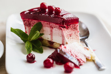 Delicious slice of red cranberry cake with berries  on white table with  broken piece of a spoon