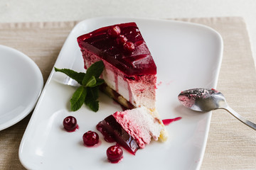 Delicious slice of red cranberry cake with berries  on white table with  broken piece of a spoon