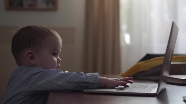 A baby son clicking on the laptop keyboard sitting on mother laps close up. The child is accustomed to gadgets. Busy young mother working at home. Freelance concept
