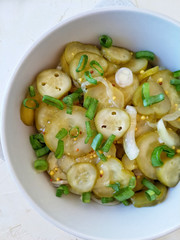 Salad of pickled cucumbers with onions in a bowl, on a light background top view. 