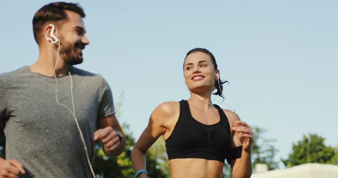 Close up of the sporty young Caucasian couple jogging together with music in headphones at the tadium on a nice summer day.