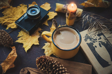 Yellow mug with autumn leaves, a book and candles. The concept of comfort and warmth.
