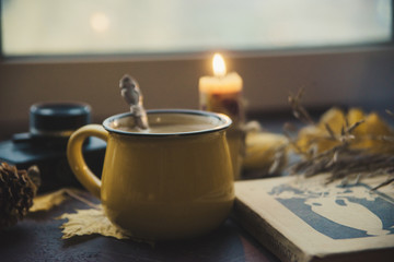 Yellow mug with autumn leaves, a book and candles. The concept of comfort and warmth.