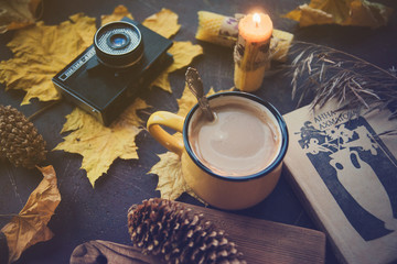 Yellow mug with autumn leaves, a book and candles. The concept of comfort and warmth.