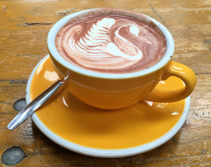 a yellow cup of chocolate art on hot chocolate on wooden table