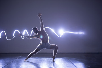 Modern Dance performer dancing with a neon blue light while making gracious moves and spectacular...