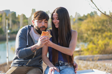Fototapeta premium Couple eating pizza outdoors and smiling.They are sharing pizza