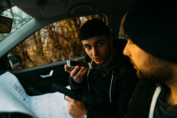 Two armed bandits sitting in a car planning their next robbery, while counting on a stopwatch the...