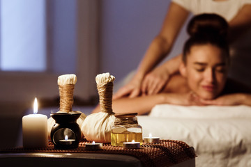 Woman relaxing in spa salon with herbal bags on wooden tray