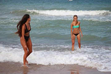 Two cute funny young girls are walking along the beach, laughing, having fun, crazy emotions, with bikini