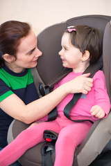 Mother securing daughter in the car seat, isolated with clipping path