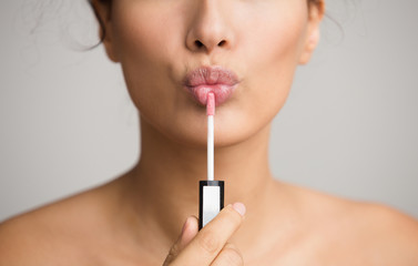 Young woman applying lip gloss on her lips - obrazy, fototapety, plakaty
