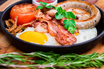 Nutritious meal with fried egg, sausage, bacon, tomato and sauce in frying pan
