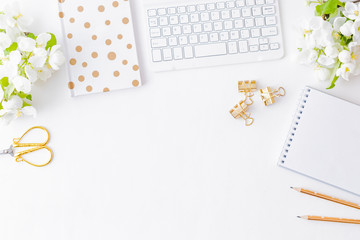 Flat lay blogger or freelancer workspace with a notebook, keyboard and white spring flowers on a white table