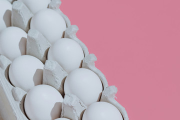 White chicken eggs in a cardboard package with empty space, on a pink coral background