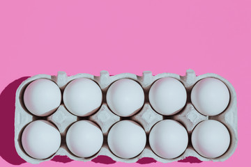 White chicken eggs in a cardboard package with empty space, on a pink background