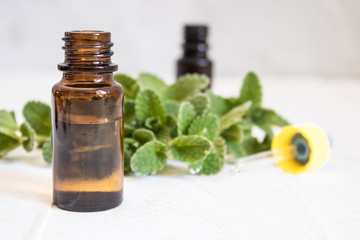 A bottle of mint essential oil with fresh mint leaves in the background.